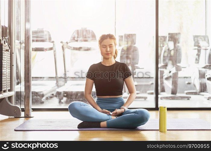 Young Asian woman practicing yoga sitting in meditation exercise, rest calm relax pose working out wearing sportswear, meditation session indoor sport club interior.