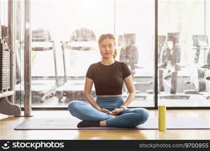 Young Asian woman practicing yoga sitting in meditation exercise, rest calm relax pose working out wearing sportswear, meditation session indoor sport club interior.