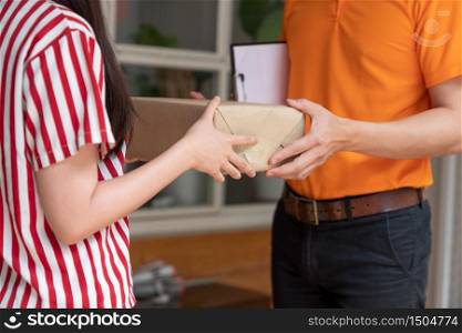 Young Asian woman receiving package box from delivery man in orange uniform at her home.Courier service.