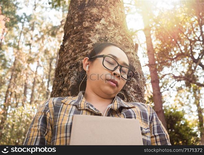 Young Asian woman relaxation and listening to music on earphone with closed her eyes in the garden on vacation day.