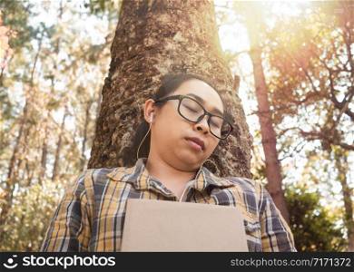 Young Asian woman relaxation and listening to music on earphone with closed her eyes in the garden on vacation day.