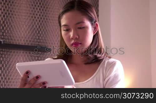 Young Asian woman relaxing in bedroom at home, college student studying, pretty Chinese girl using ipad digital tablet for internet, email, test. Happy people, technology, lifestyle, fun, leisure
