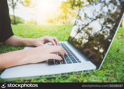 Young asian woman&rsquo;s legs on the green grass with open laptop. Girl&rsquo;s hands on keyboard. Distance learning concept. Happy hipster young asian woman working on laptop in park. Student studying outdoors.