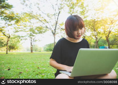 Young asian woman&rsquo;s legs on the green grass with open laptop. Girl&rsquo;s hands on keyboard. Distance learning concept. Happy hipster young asian woman working on laptop in park. Student studying outdoors.