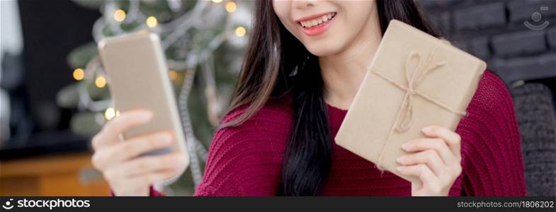 Young asian woman selfie video call online with friends and show gift box in Christmas day on phone at home, social distancing, new normal, female video conference, communication and holiday concept.