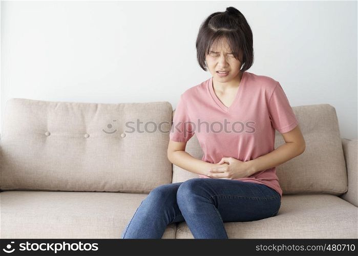 Young asian woman sit on sofa in the living room. she having painful stomachache.