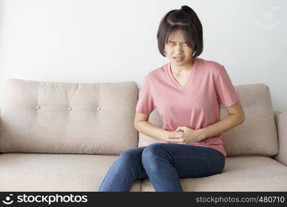 Young asian woman sit on sofa in the living room. she having painful stomachache.