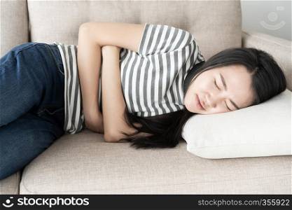 Young asian woman sit on sofa in the living room, women having painful stomachache.