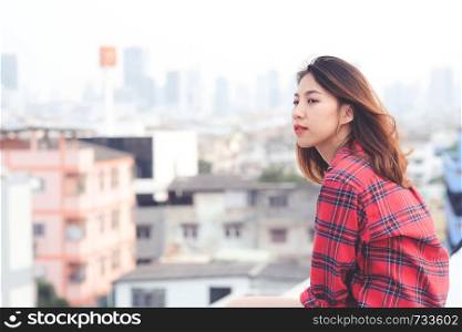 Young asian woman sitting and smiling at rooftop outdoor in urban city background, happy lifestyle