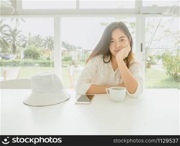 Young asian woman sitting in cafe at table with enjoying hot coffee, Front view beautiful girl looking at camera in coffee shop and touching her chin with hand.
