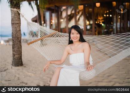 Young Asian woman sitting on hammock relax on beach, Beautiful female happy relax near sea. Lifestyle women travel on beach concept.