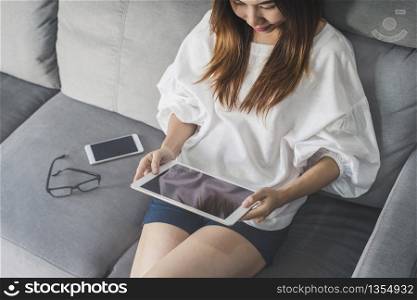 Young asian woman sitting on sofa and using tablet at home. Young asian woman using tablet at home