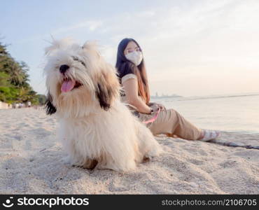 Young asian woman sitting with her fluffy puppy on the beach at Pattaya. New Normal lifestyle.