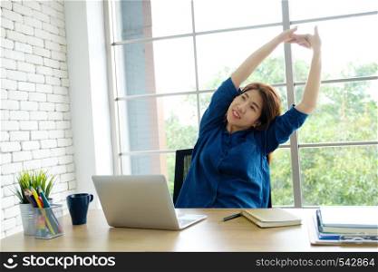 Young asian woman stretching body for relaxing while working with laptop computer at her desk, home office lifestyle, business situation