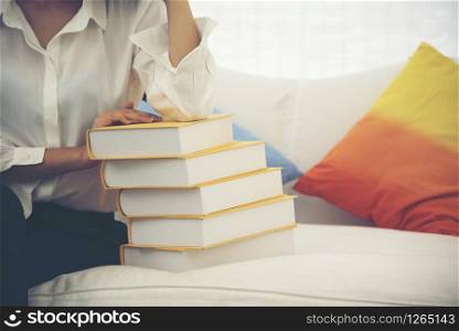 Young Asian Woman student university holding text book on her hands sitting on sofa with colorful pillow. Study hard to get a better grade. Education Concept