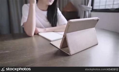 Young asian woman study online by watching tablet, home school tuition, stay at home concept, self discipline on education, hand writing down on notebook, taking lecture from online class course