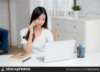 Young asian woman talking phone and work from home with laptop computer, freelance using notebook to internet online and speak on smartphone, domestic life, business and communication concept.