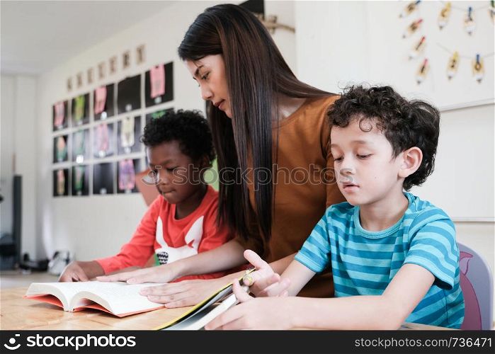 Young asian woman teacher and American, African boys in kindergarten classroom, preschool education concept