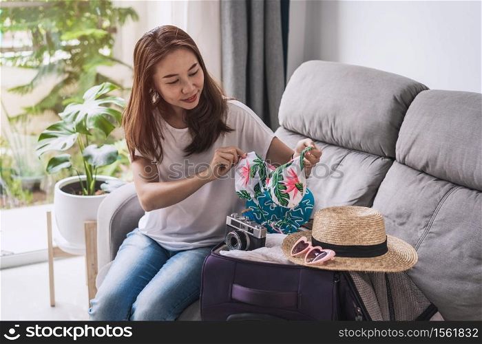 Young asian woman traveler packing her suitcase and planning for the summer vacation, Travel concept