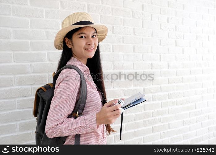 Young asian woman traveler with backpack holding vintage camera and map standing in white room with copy space, people summer holiday vacation background concept