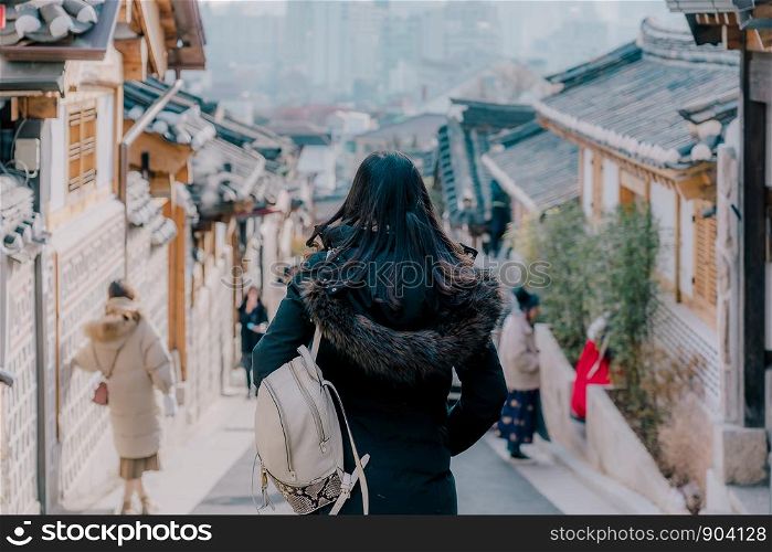 Young asian woman traveler with backpack traveling into the traditional Korean style architecture at Bukchon Hanok Village in Seoul, South Korea.