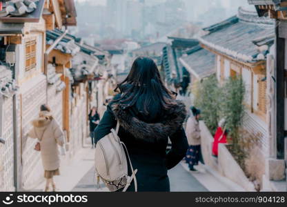 Young asian woman traveler with backpack traveling into the traditional Korean style architecture at Bukchon Hanok Village in Seoul, South Korea.