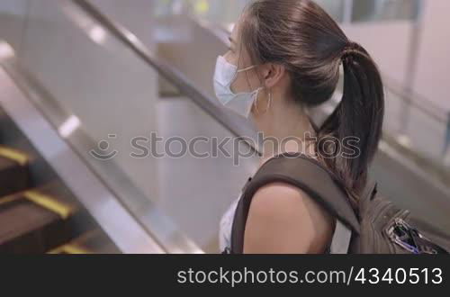 Young asian woman traveling by herself during covid19 pandemic, wear protective face mask preventing from infectious diseases, standing on escalator holding handrail, risk of contaminated objects