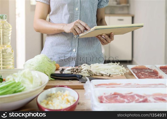 Young asian woman using her touchpad and reading recipes while cooking in the kitchen. Young woman using her touchpad in the kitchen
