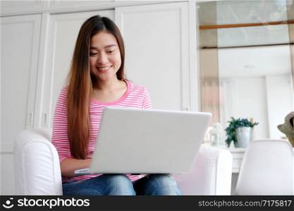 Young asian woman using laptop computer in casual while sitting in white room at home background, working at home, people and technology, lifestyles, online education, business concept