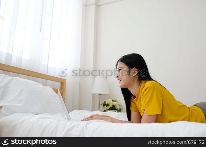Young asian woman using laptop computer on bed in her bed room background with copy space, working at home, people and technology, lifestyles, education, business concept