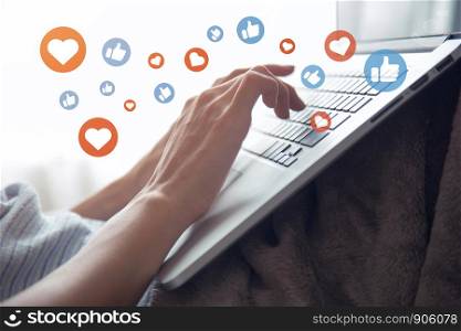 Young asian woman using laptop computer sharing and commenting on social network application with heart and thumb up icon, modern lifestyle or communication technology concept