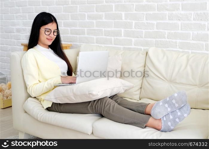 Young asian woman using laptop computer sitting on sofa at home living room background, working at home, people and technology, lifestyles, education, business concept