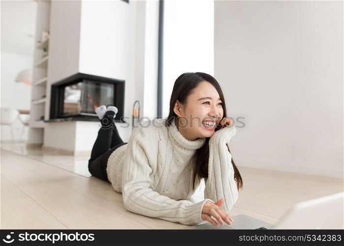young Asian woman using laptop in front of fireplace on cold winter day at home