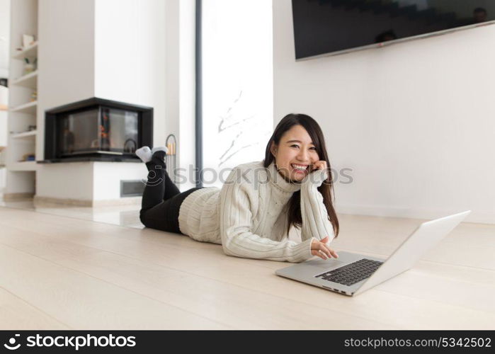 young Asian woman using laptop in front of fireplace on cold winter day at home