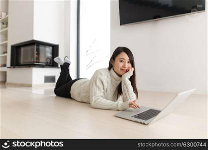 young Asian woman using laptop in front of fireplace on cold winter day at home