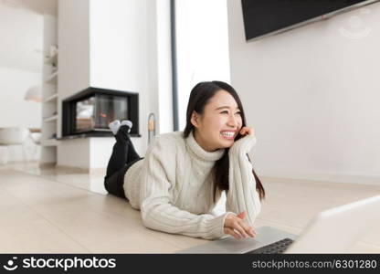 young Asian woman using laptop in front of fireplace on cold winter day at home