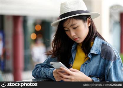 Young asian woman using phone standing in front of cafe in the city outdoors background, people working outdoors with technology, lifestyle