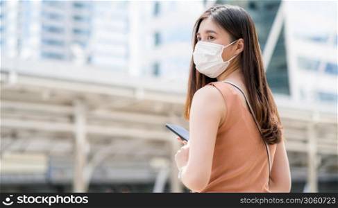 Young Asian woman using smart mobile phone in outside big city at Covid19 outbreak, Infection and Pandemic, commuter and transportation, social distancing and new normal concept