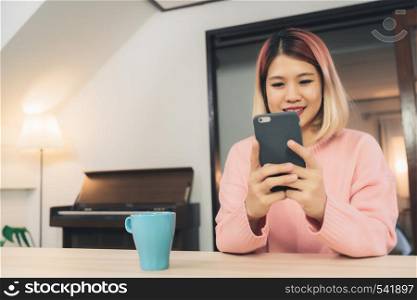 Young Asian woman using smartphone while lying on the desk in her living room. Happy female use phone for texting, reading, messaging and buying online at home. Lifestyle woman at home concept.