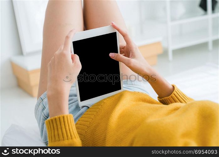 Young Asian woman using tablet mock up blank black screen in her bedroom alone by swiping it with her finger in the warm light sunshine day. Woman swipe on tablet in the bedroom.