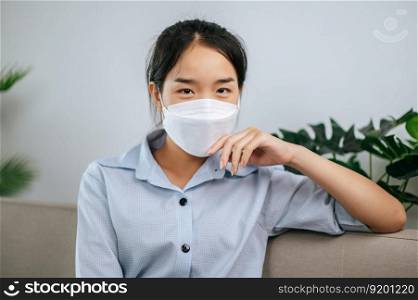 Young asian woman wearing face mask sitting on sofa in the living room, she reading book during quarantine covid-19 self isolation at home