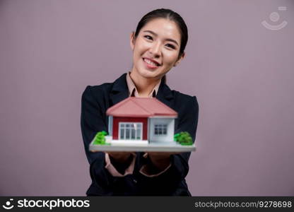 Young Asian woman wearing formal suit, holding and showcasing house model on isolated background. Ideal for housing advertisement, home insurance promotions, or customizable copy space. Enthusiastic. Young Asian woman wearing formal suit holding house model. Enthusiastic