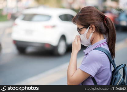 young Asian woman wearing N95 respiratory mask protect and filter pm2.5 (particulate matter) against traffic and dust city. healthcare and air pollution concept