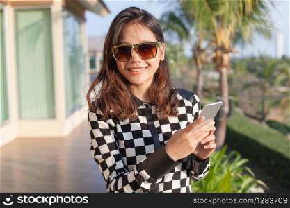 young asian woman wearing sun glasses and smart phone in hand toothy smiling face
