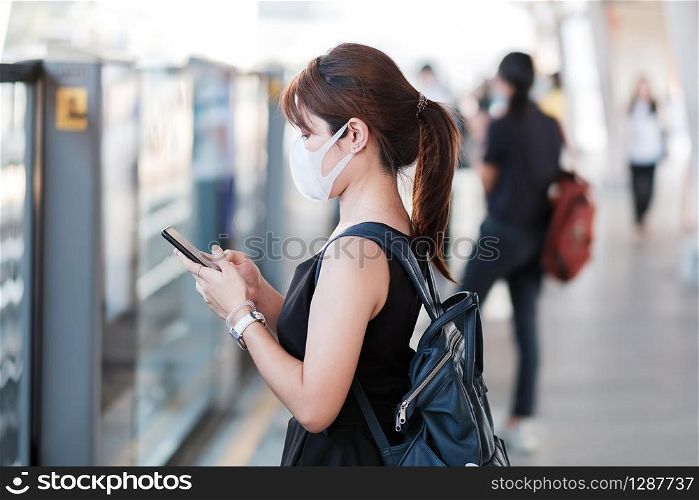 young Asian woman wearing surgical face mask against Novel coronavirus or Corona Virus Disease (Covid-19) at public train station. Hygiene, Healthcare and infection concept