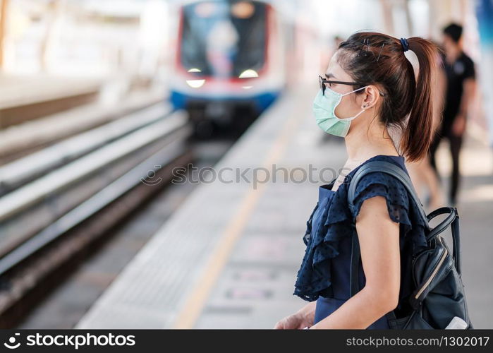 young Asian woman wearing Surgical face mask against Novel coronavirus or Corona Virus Disease (Covid-19) at public train station. Hygiene, Healthcare and infection concept