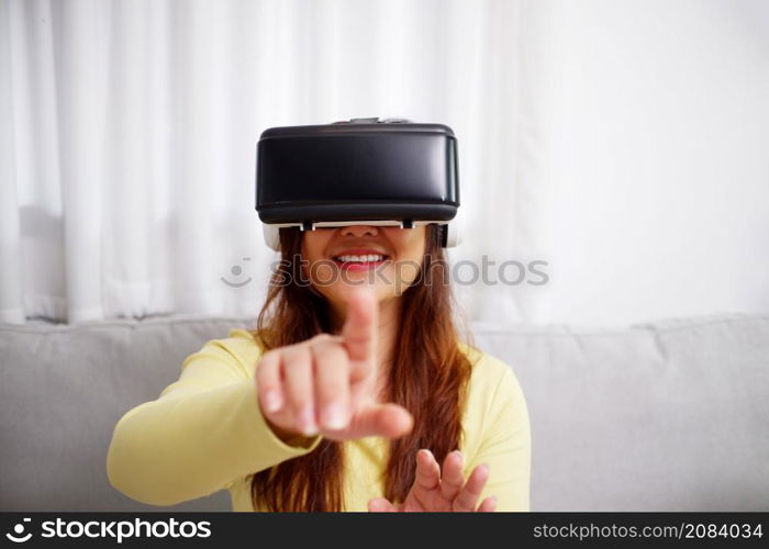 Young asian woman wearing virtual reality glasses, hand touching the air. VR headset. VR concept. Home entertainment.