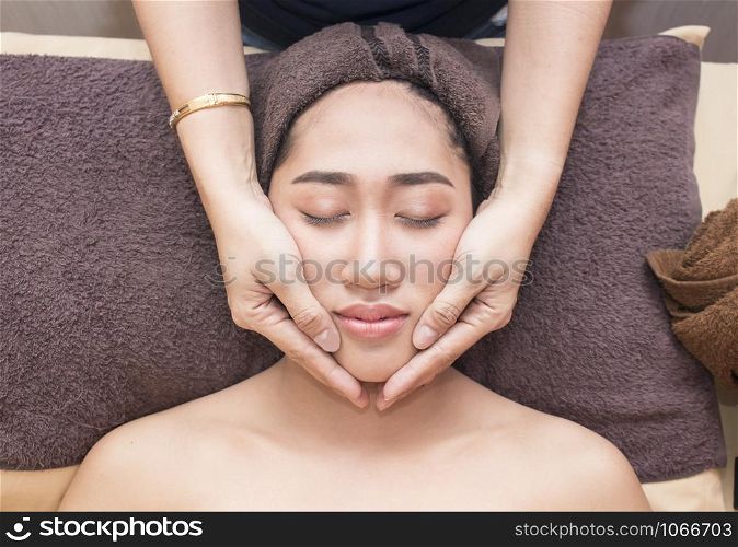 young asian woman with closed eyes getting a massage on her face in spa treatment