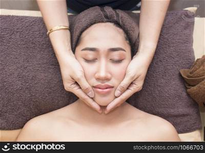 young asian woman with closed eyes getting a massage on her face in spa treatment