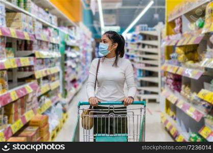 young asian woman with shopping cart in supermarket department store and her wearing medical mask for prevention coronavirus(covid-19) pandemic. new normal concept